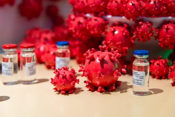 Representación del virus COVID-19 en modelo de plástico rojo, con representación de dosis de vacunas a su alrededor.